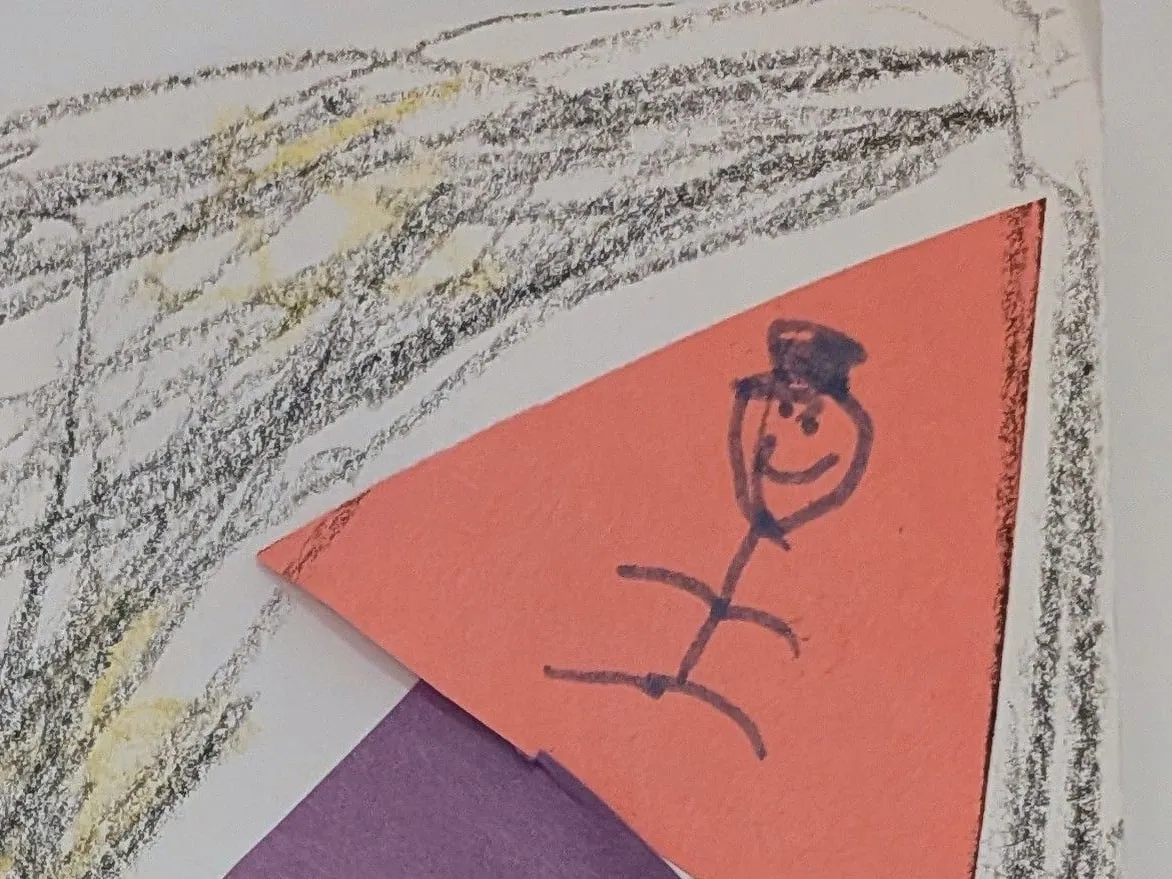 A child’s crayon drawing of a smiling stick figure on orange paper