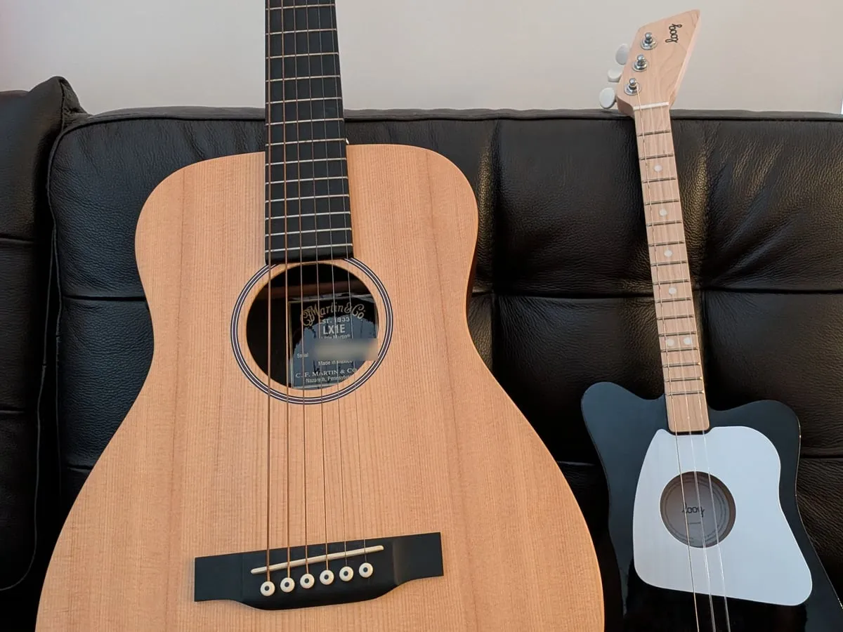 A full-size acoustic guitar next to a small child’s guitar on a couch
