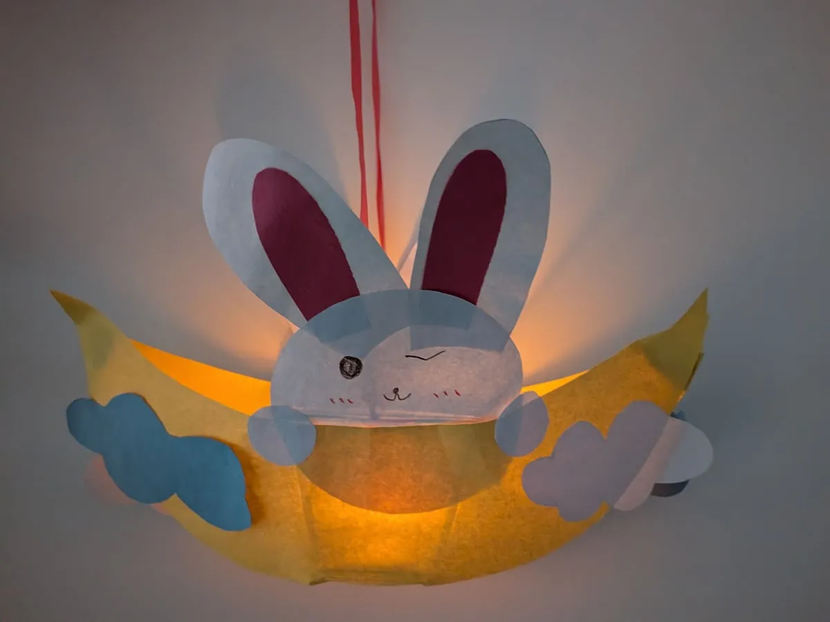 A glowing paper lantern shaped like a bunny sitting in a crescent moon